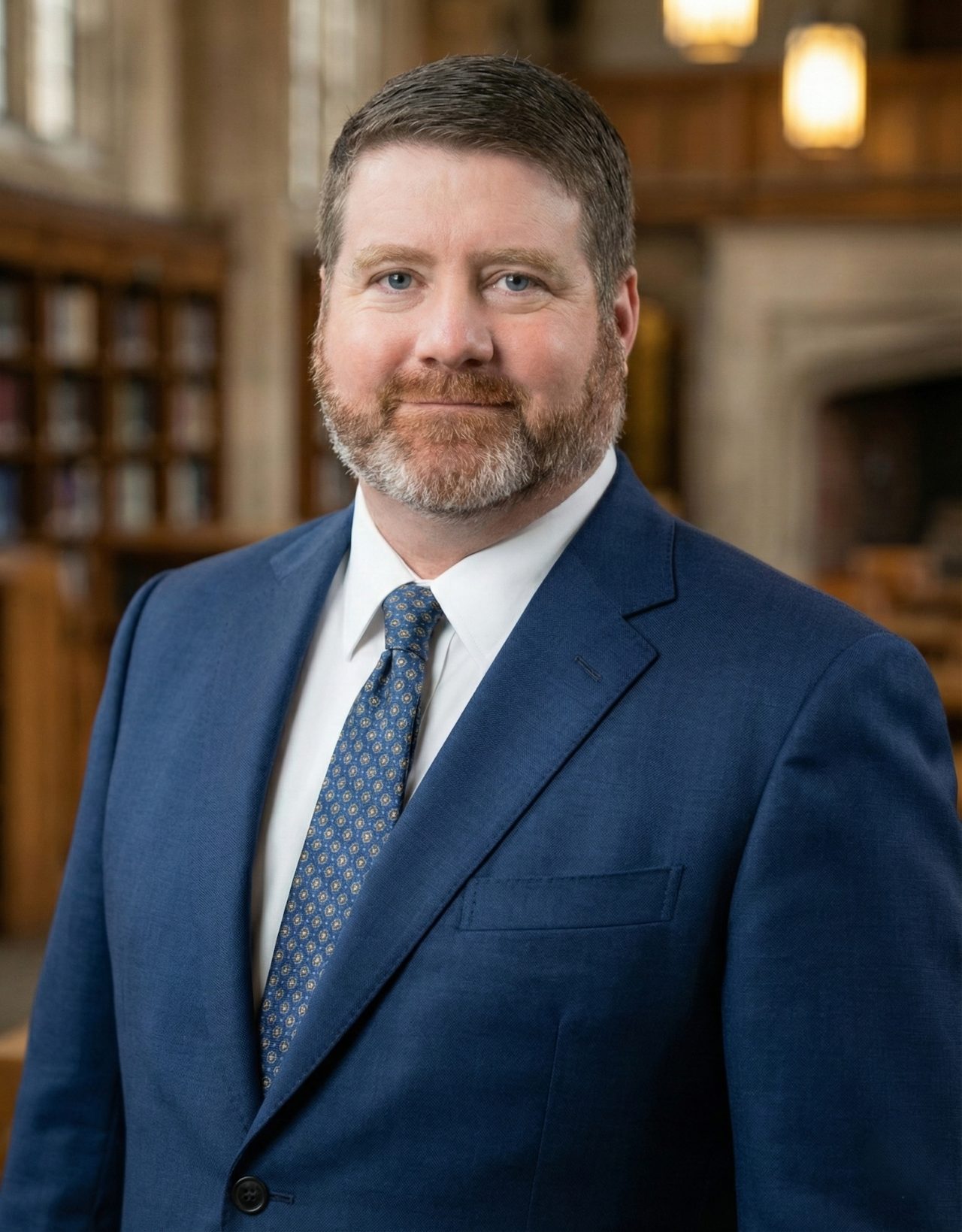 Portrait of Dr. Lane Freeman in a navy suit and blue tie, standing in a library.